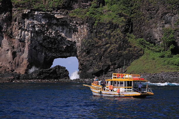 Rock formation and boat, Fernando de Noronha Fernando de Noronha, Brazil - May 17, 2011: An excursion boat with tourists anchored in front of the rock formation known as Ponta da Sapata.  bioreserve photos stock pictures, royalty-free photos & images