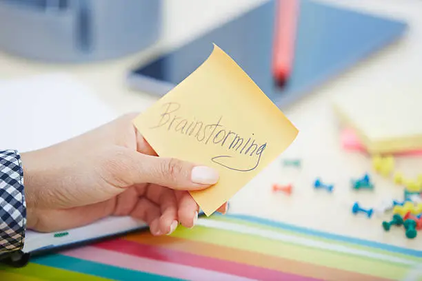 Human hand holding adhesive note with Brainstorming text