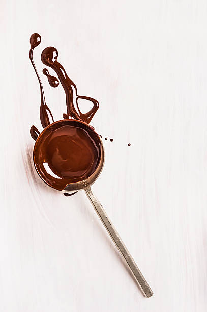 spoon with liquid chocolate on white wooden background spoon with liquid chocolate on white wooden background fudge stock pictures, royalty-free photos & images