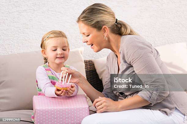 Mother And Daughter Sitting On Sofa Mother Lights Birthday Candles Stock Photo - Download Image Now