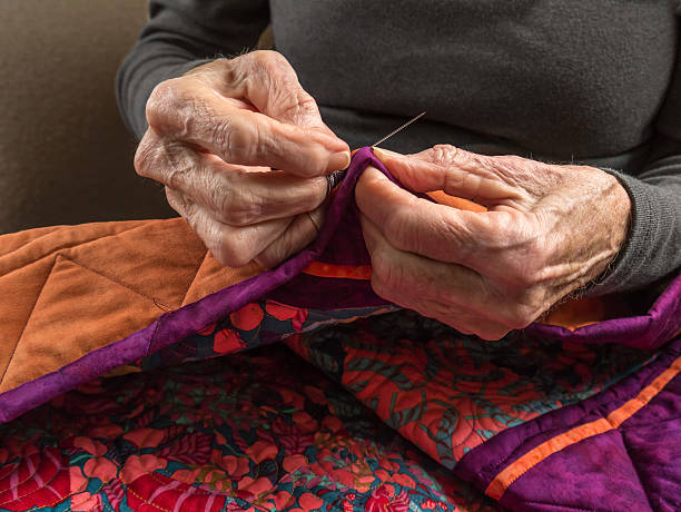 Senior Woman Expertly Stitches the Binding Onto Her Quilt stock photo