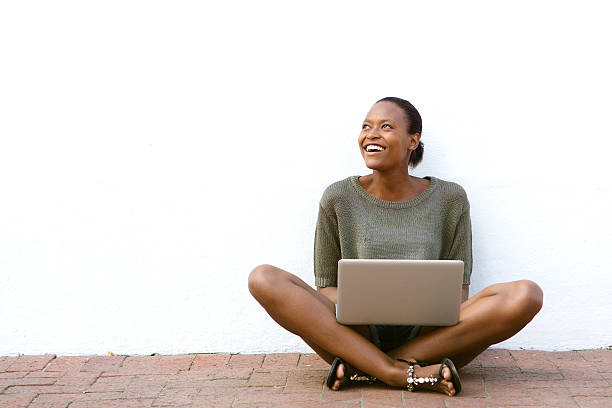 felice afro-americana donna seduta con computer portatile - sedere per terra foto e immagini stock