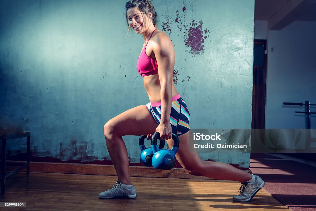 Girl doing lunge exercise Young adult caucasian girl doing lunge exercise indoor with kettlebell. Toned Image. Active Lifestyle Stock Photo