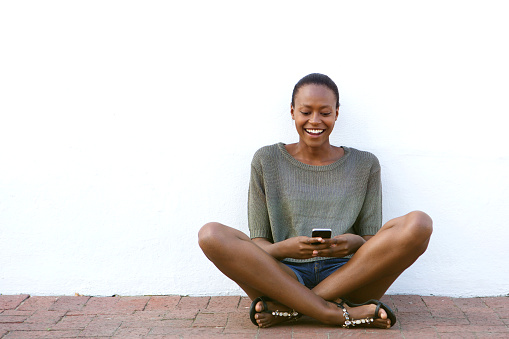 Portrait of happy young woman sitting on sidewalk with cell hone