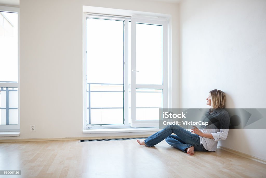 Young woman in her new apartment Just moved in: beautiful young woman finally sitting down and relaxing -  having a drink in her brand new modern apartment Apartment Stock Photo
