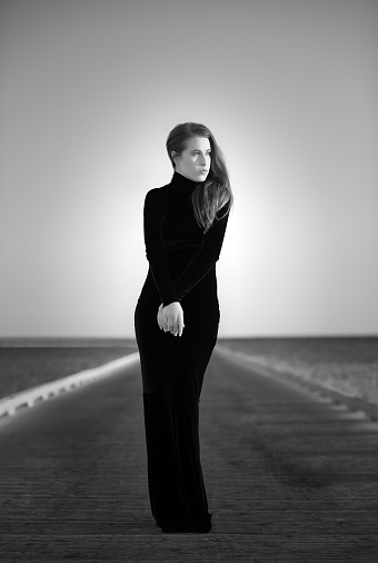 elegant woman in long black dress posing on bridge.