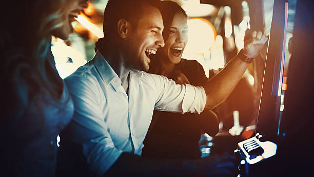 Group of people having fun in casino. Closeup side view of a group of young adults playing slots in casino and having fun on weekend night.All standing by one machine and playing.Two couples on double date casino stock pictures, royalty-free photos & images