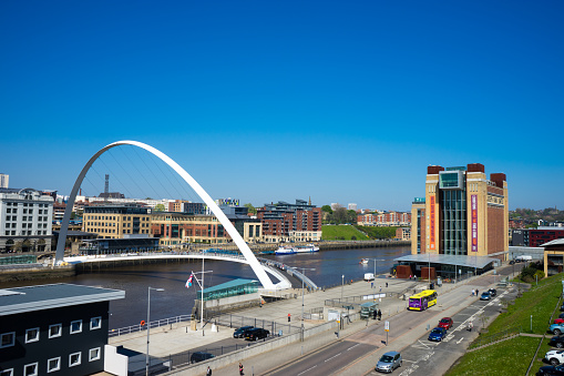 Newcastle, UK - May 9, 2016: The Gateshead Millennium Bridge is a pedestrian and cyclist tilt bridge spanning the River Tyne in England between Gateshead's Quays arts quarter on the south bank, and the Quayside of Newcastle upon Tyne on the north bank.  A Quaylink bus is on the road, and the Baltic Centre for Contempory Art is in shot.