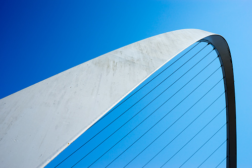 The Gateshead Millennium Bridge is a pedestrian and cyclist tilt bridge spanning the River Tyne in England between Gateshead's Quays arts quarter on the south bank, and the Quayside of Newcastle upon Tyne on the north bank.  The image is an abstract take on the bridge, set against a blue sky.