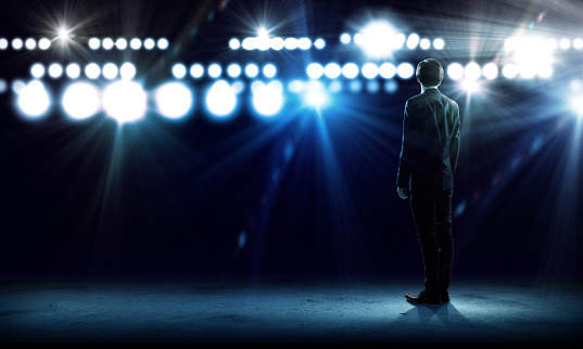 Rear view of businessman standing in lights of stage