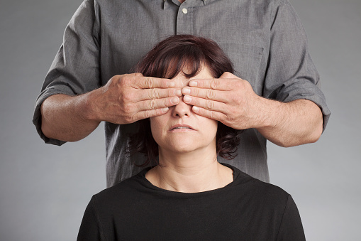 Man standing behind woman covering her eyes