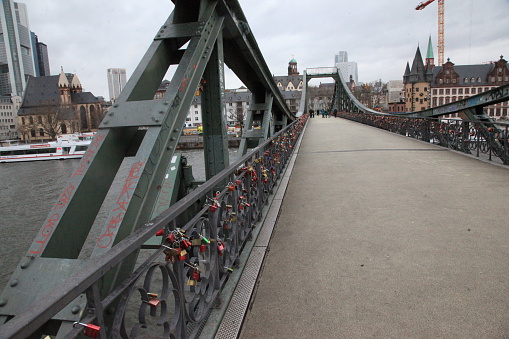 Frankfurt, Germany – December 11, 2014: Pedestrians on Eiserner Steg bridge where love locks tied are to the fence of the bridge and St. Paul's Church appears in the background. 