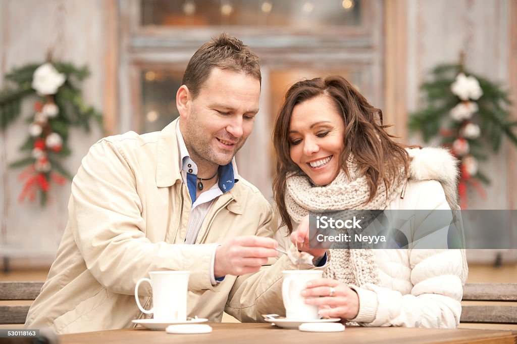 Romantic Couple at Christmas Time Couple sitting at table outdoors in front the restaurant and drinking tea. Horizontal color image. Ljubljana, Slovenia. Christmas Stock Photo