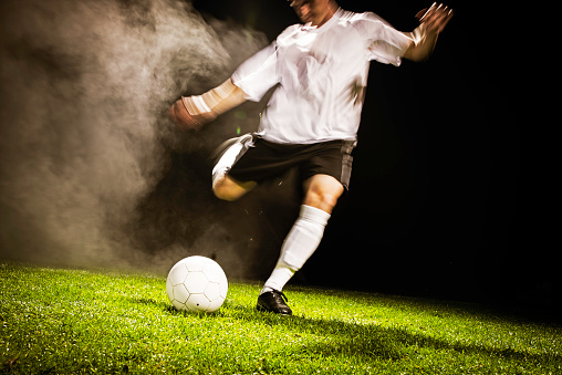 Soccer player kicks ball with full power at night.