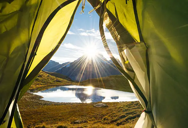 View out of a tent in the Bernese Oberland, a famous tourist spot in Switzerland. In the background are mountains and a small lake, close to the famous "Bachalpsee" in Grindelwalds mountains. It's autumn and there is Snow in the mountains in the background.