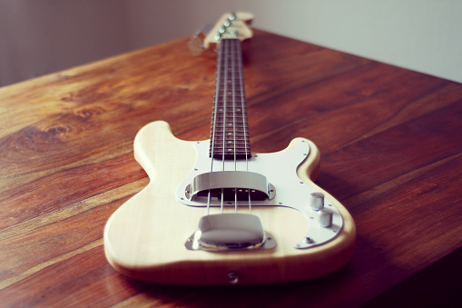 Berlin, Germany - November 06, 2014: Wooden Fender bass guitar shot on a wooden table in Berlin, Germany. The bass guitar has a natural finish.