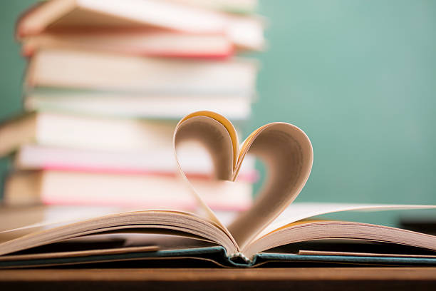 I love to read!  A heart shape created with open hardback book pages in foreground with a large stack of books and green chalkboard in background.  School classroom or library setting.  Education themes.   No people.