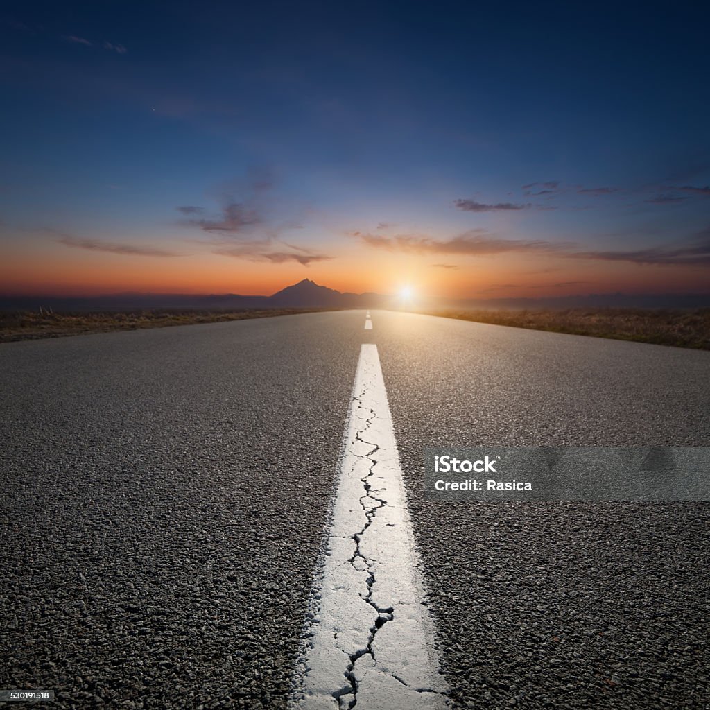 Driving on open road towards the mountain at sunrise Empty highway leading to the mountains through the desert against the rising sun at beautiful sunrise. Road Stock Photo