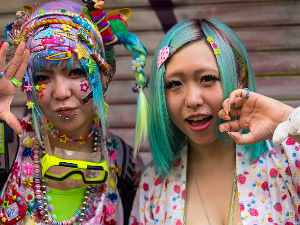 Cosplay girls at Harajuku'sTakeshite Street in Tokyo Tokyo, Japan - August 17, 2014: Front view of two women dressed in Cosplay stile while commutating with other Cosplay people in front of them. One is lake fairy tale character, with big swimming neckless, many brooch, parsing’s and chewing gum. She has some droving’s on her face. The other one has only two brooches on her hair, which is painted too.  The background is outside surface of a building. tokyo harajuku stock pictures, royalty-free photos & images