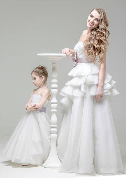 Portrait of 18 months old baby girl smiling and looking at camera. Small girl wearing flower wreath and trying on wedding dress at bridal boutique.