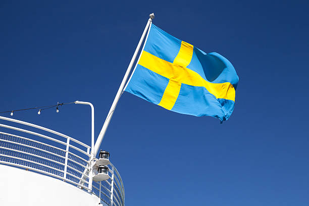 Swedish flag mounted on the stern of white passenger ship waving over blue sky background