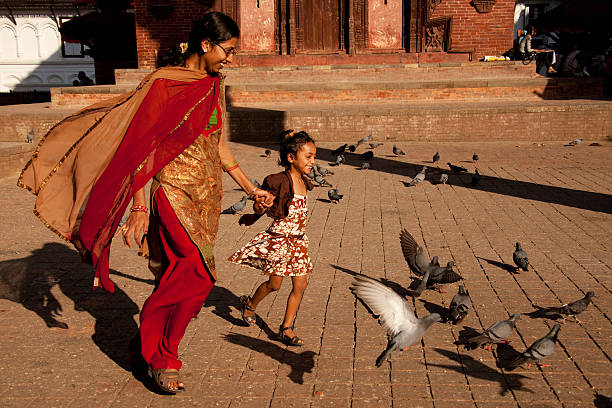 Mother and daughter chasing pigeons in Kathmandu. Kathmandu, Nepal - October 10, 2011: Mother in traditional dress, and her daughter, chase pigeons in Durbar Square, Kathmandu, Nepal, with smiles on their faces. pigeon family stock pictures, royalty-free photos & images