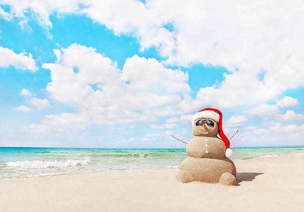sandy bałwan śniegowy w santa hat na plaży. boże narodzenie koncepcja - new year zdjęcia i obrazy z banku zdjęć