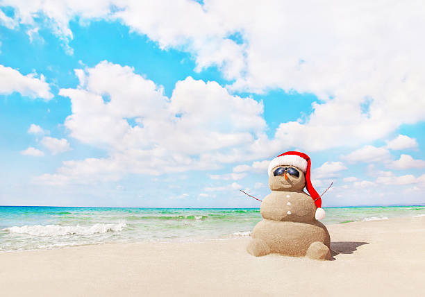 boneco de neve areia no chapéu do pai natal na praia. conceito de natal - christmas beach sun tropical climate imagens e fotografias de stock