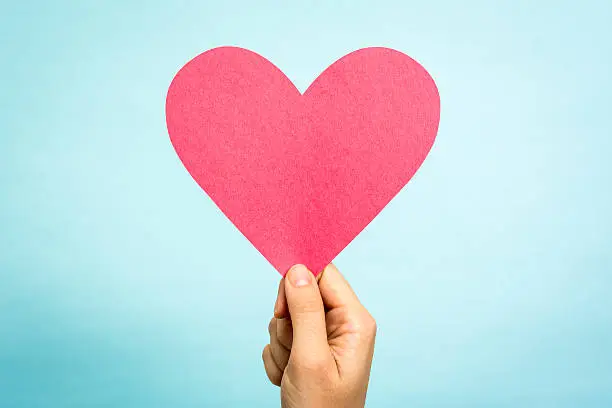 Photo of Hand showing big red pink heart love symbol blue background