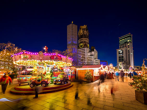 Christmas Market in Berlin, Germany Berlin, Germany - November 25, 2013: People walking past a carousel sitting in the middle of the Christmas market in Tauentzienstrasse, a major shopping district in Berlin, Germany. The Kaiser Wilhelm Memorial Church can be seen in the background. kaiser wilhelm memorial church stock pictures, royalty-free photos & images