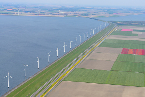 Aerial view of wind turbines on the coast with the highway A6 and various colors of tulip flower fields in Flevoland, The Netherlands. Each year during spring different areas in Holland are colored vividly by growing flower bulbs.