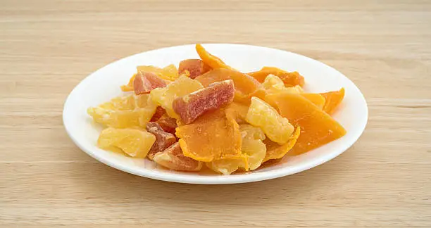 A plate with pineapple, mango and papaya sugared dried fruit on wood table top.