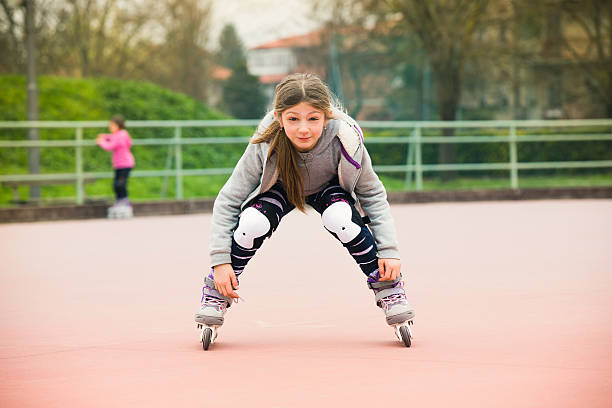 Cute little child girl on roller skates rollerblading fast at park in summer day.