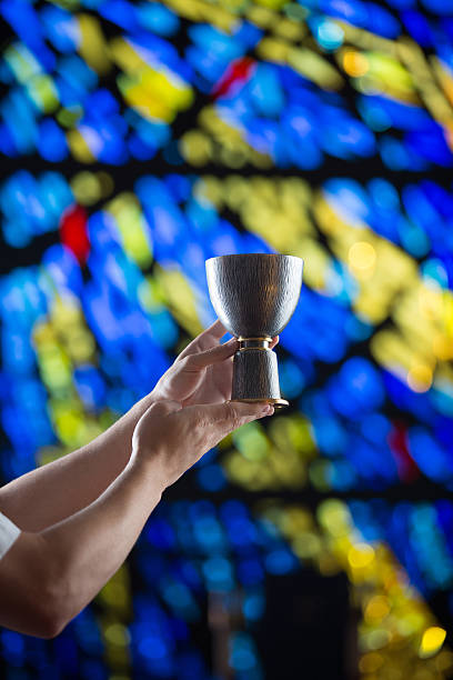 Chalice and Stained Glass Metal chalice held during a religious ceremony with stained glass window in the background. anglican eucharist stock pictures, royalty-free photos & images
