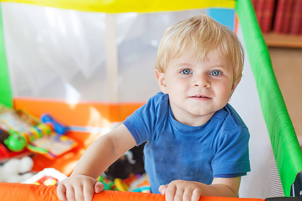 cute little baby boy playing in colorful playpen, indoors - babybox stockfoto's en -beelden