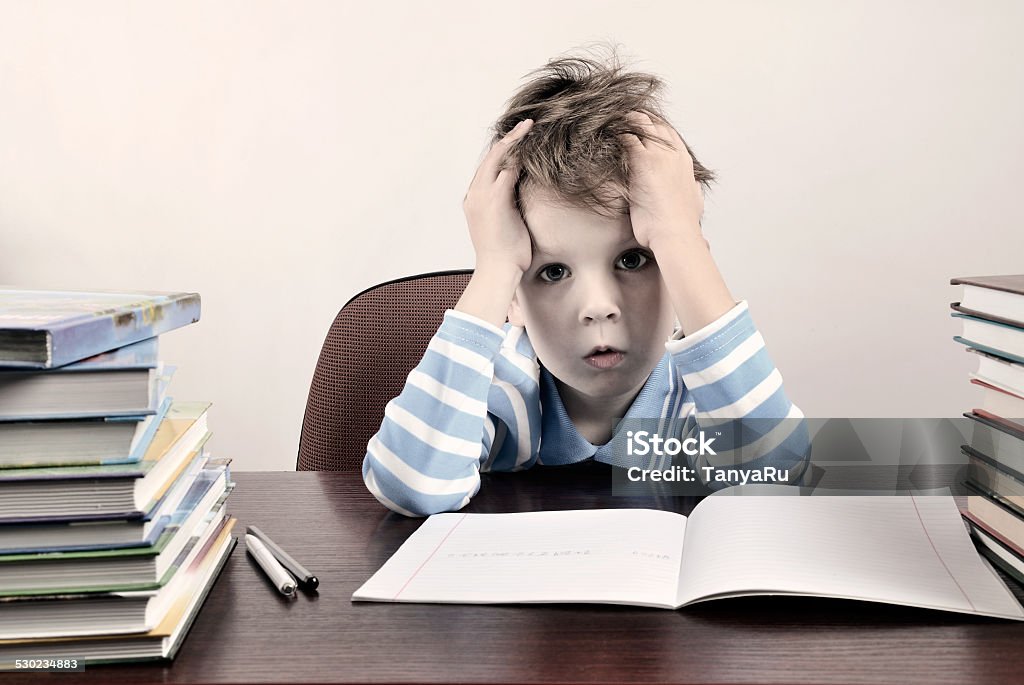 tinted image tired boy sitting at desk and holding hands tinted image tired boy sitting at a desk and holding hands to head horizontal Boys Stock Photo