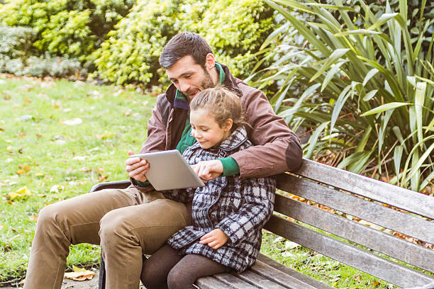 istock Father And Daughter Using Tablet Sitting On A Bench 530240627