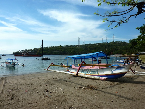 Senggigi, Indonesia - November 11, 2013: Panboats moored at Senggigi harbour. Senggigi is the main tourist strip of Lombok, stretched out along the several kilometers of the beachfront, just to the north of Mataram city. In the background, local people walking on the beach.