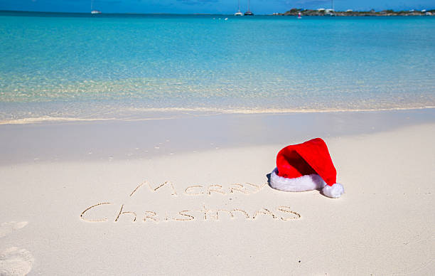 istock Merry Christmas written on beach white sand with xmas hat 530250039