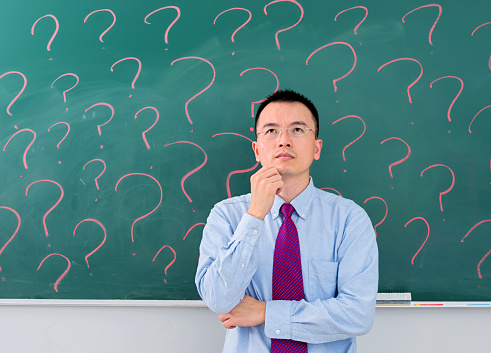 Asian businessman in front of blackboard with question marks.