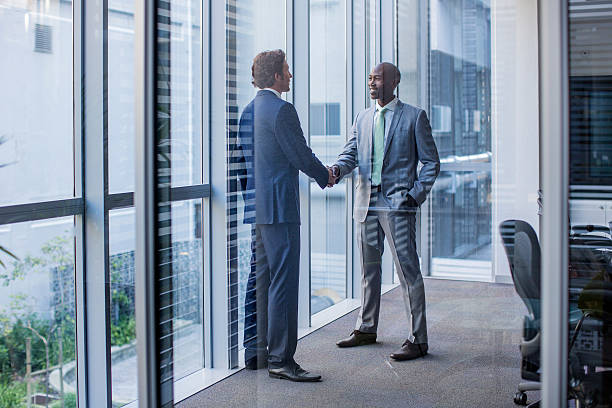 multi-ethnic businessmen shaking hands in office - full length windows stock-fotos und bilder