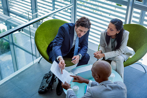 Businesspeople discussing over documents in office High angle view of multi-ethnic businesspeople discussing over documents in office formal businesswear stock pictures, royalty-free photos & images