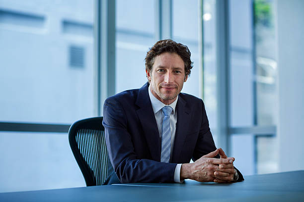 confident businessman sitting at conference table - formelle geschäftskleidung stock-fotos und bilder