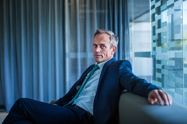 businessman relaxing on sofa in office lobby - gray hair immagine foto e immagini stock