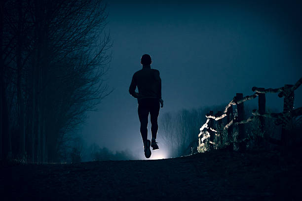 Running in the night A man running on a dirty road during the night near a river in the country running jogging men human leg stock pictures, royalty-free photos & images