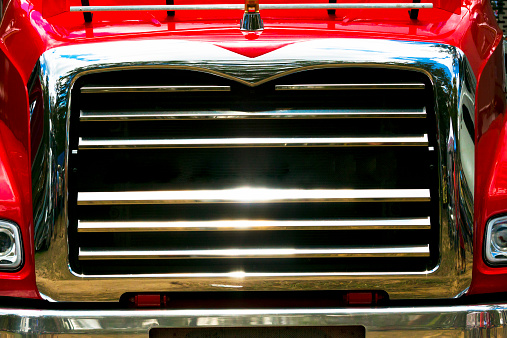 Closeup front view of old red truck chrome radiator grille in sunshine, full frame horizontal composition