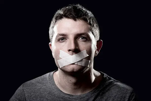attractive young man with mouth and lips sealed on tape to prevent from speaking free keeping him mute and censored in freedom of speech and expression concept