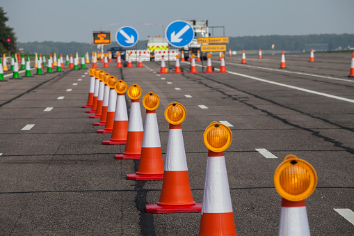 roadworks and trafic cones with blue and white arrow road signs. The trafic cones have yellow lamps on. There are also green trafic cones in the picture