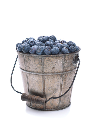 A pail full of freshly picked blueberries. Vertical format isolated on a white background with slight reflection.