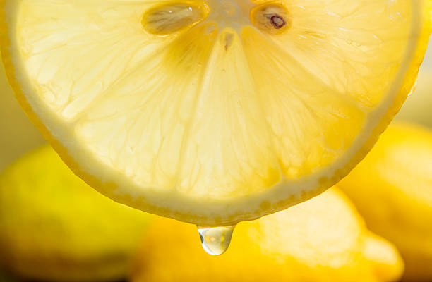 teil einer scheibe zitrone mit saft mit tropfenmuster hängen - zitronensaft stock-fotos und bilder